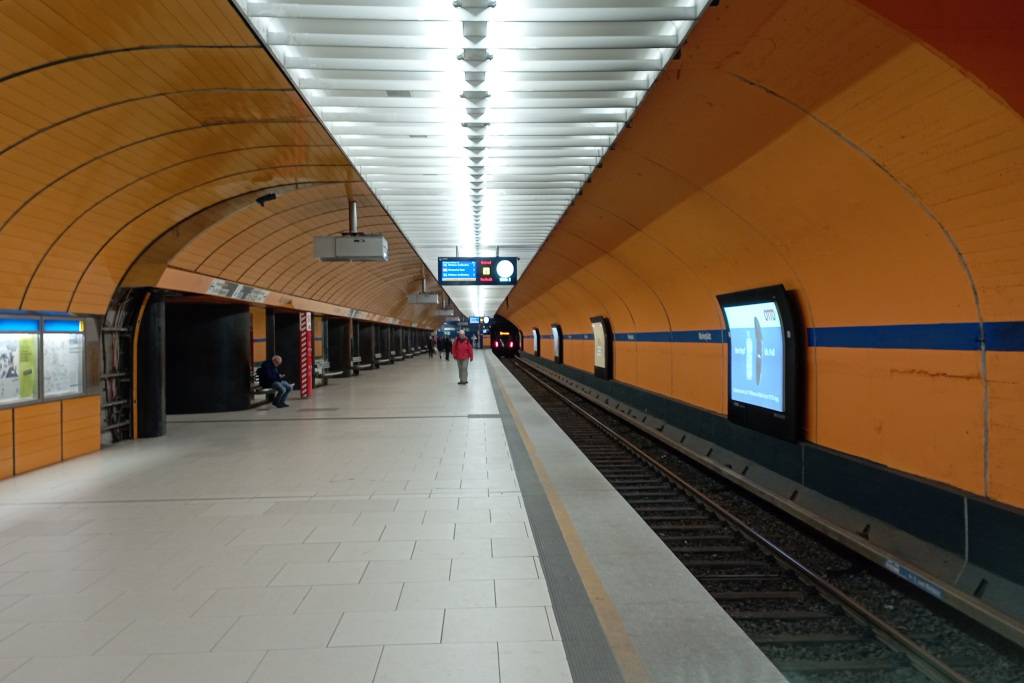 U-Bahnhof Marienplatz Fahrtichtung Sendlinger Tor. Die Wnd hinter dem Gleis (rechts) ist oarnge gestrichen. Der Bahnsteig ist - wie gehabt - orange gekachelt. Wenige Fahrgäste.